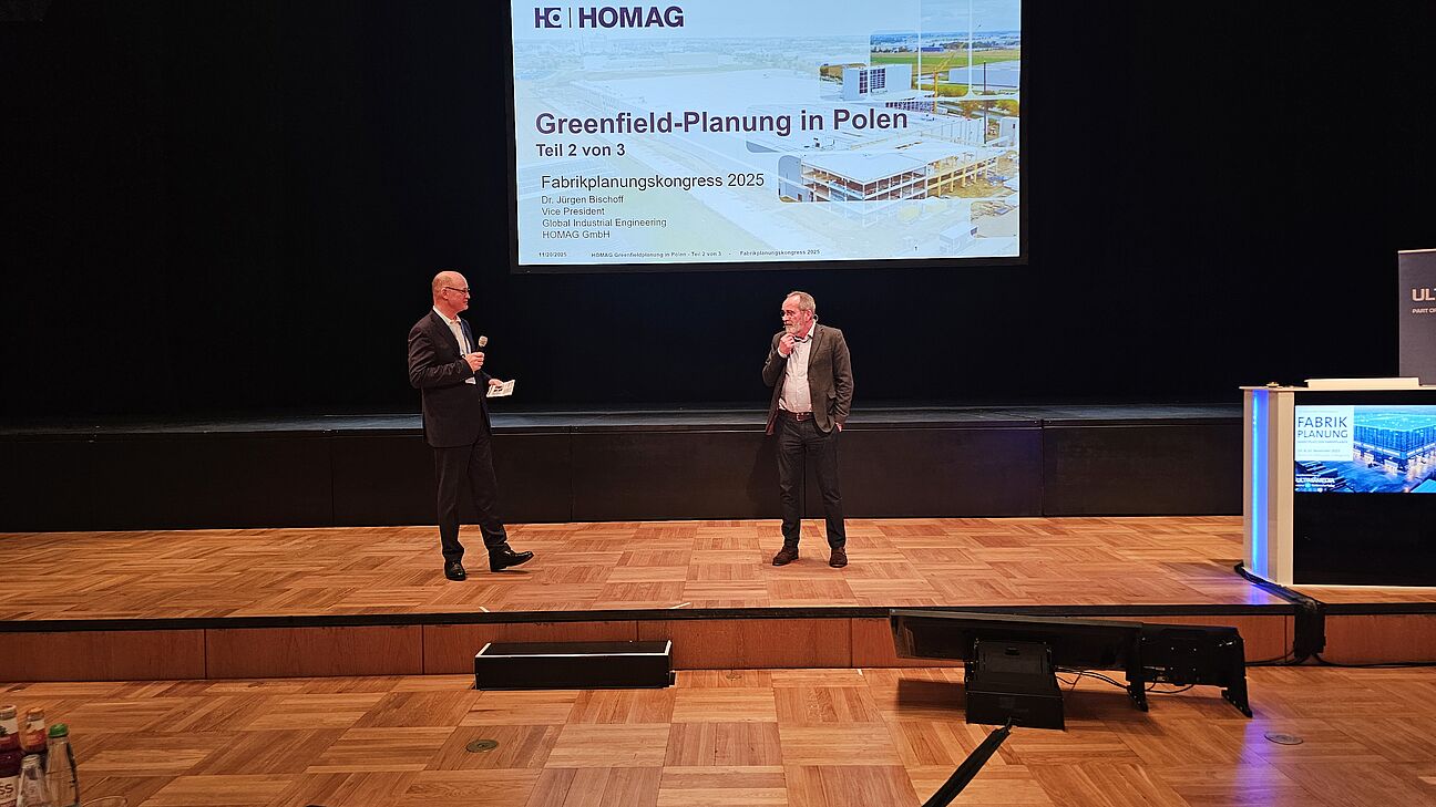 Dr. Jürgen Bischoff auf der Bühne während seines Vortrags mit Prof. Dr. Walter Wincheringer auf dem Deutschen Fachkongress Fabrikplanung 2025