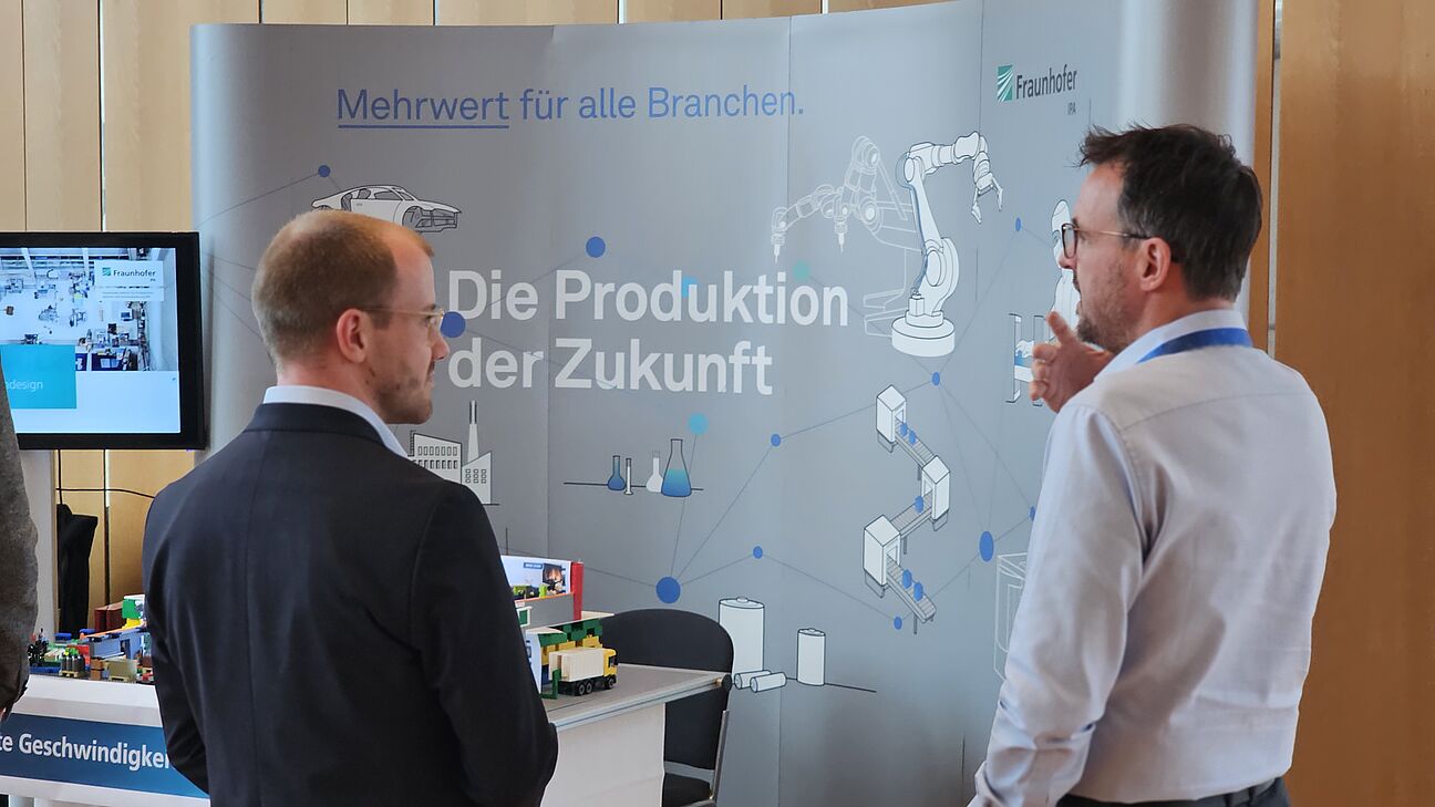 Zwei Teilnehmer am Netzwerken am Stand von Fraunhofer IPA auf dem Fachkongress Fabrikplanung 2025 in Ludwigsburg