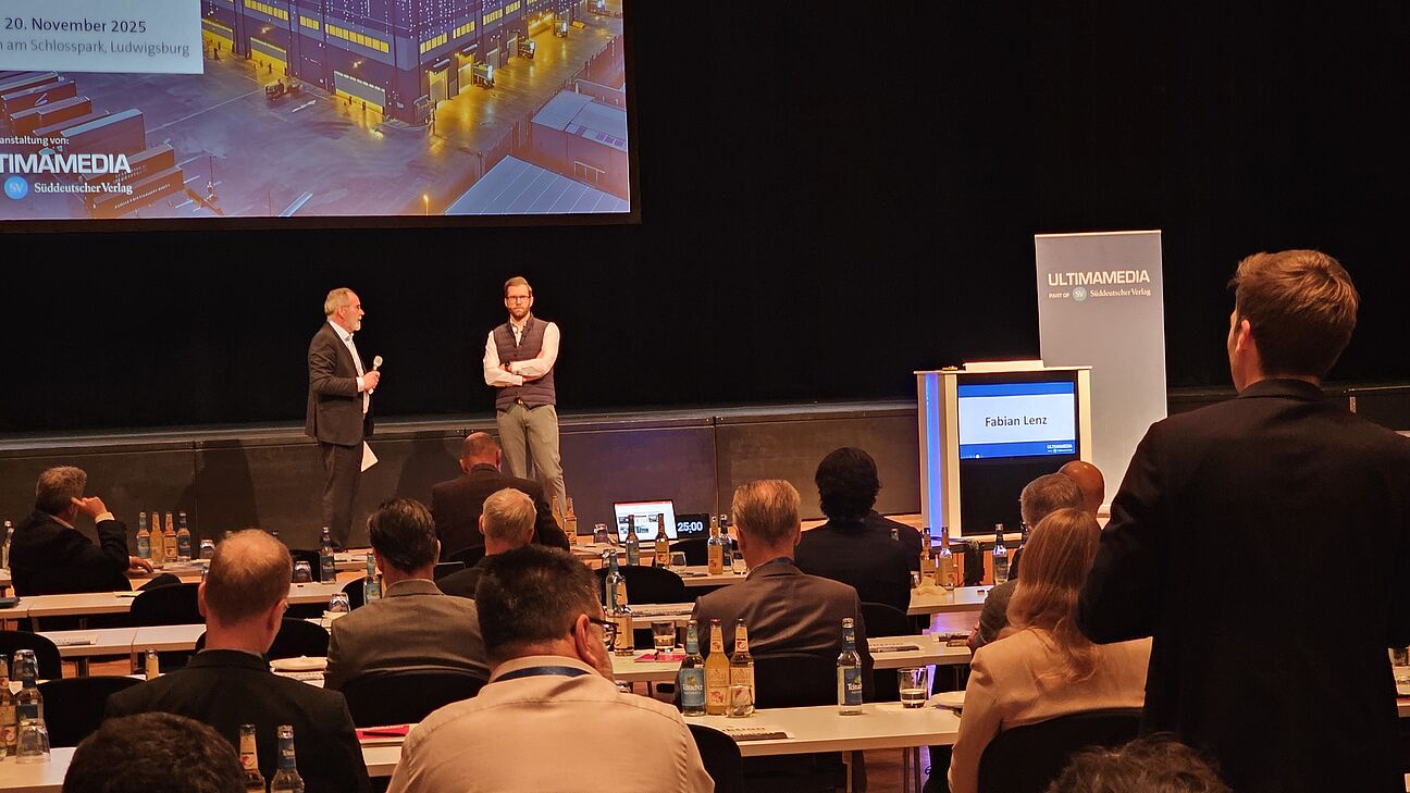 Dr. Jürgen Bischoff und Fabian Lenz auf der Bühne auf dem Fachkongress Fabrikplanung 2025. Frage aus dem Publikum. 