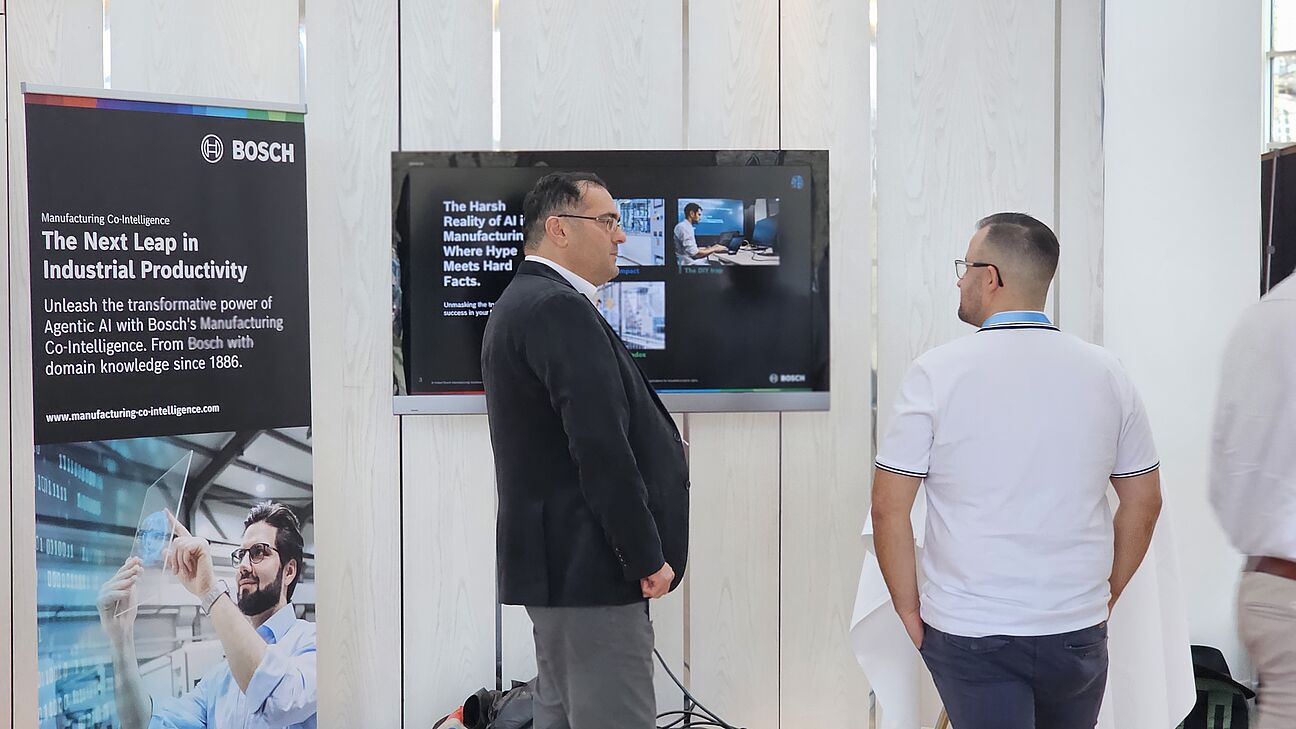 Zwei Teilnehmer am Stand von Bosch im Ausstellerbereich des Deutschen Fachkongress Fabrikplanung 2025 am Austauschen 